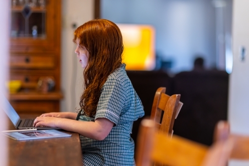 child in school uniform sitting at kitchen bench working on laptop computer - Australian Stock Image