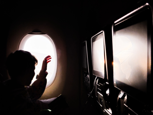 child in silhouette waving out the window of a plane - Australian Stock Image