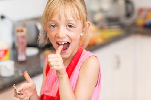 Child in the kitchen putting thumb in her mouth - Australian Stock Image