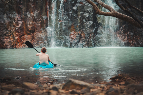 Child paddling kayak in waterhole towards waterfall at Cedar Creek Falls the Whitsundays - Australian Stock Image