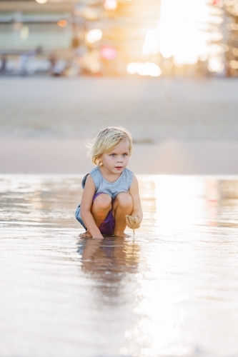 Child playing in shallow water on Gold Coast beach in golden afternoon light - Australian Stock Image