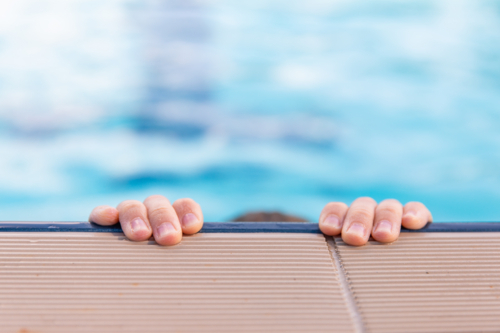 child's fingertips holding on to the edge of a public pool - Australian Stock Image