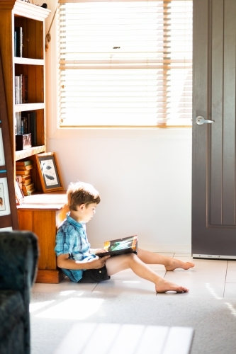 Child sitting in sunlight on the floor reading a book - Australian Stock Image