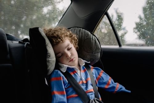 Child wearing a seat belt sleeping in the back seat of the family car - Australian Stock Image