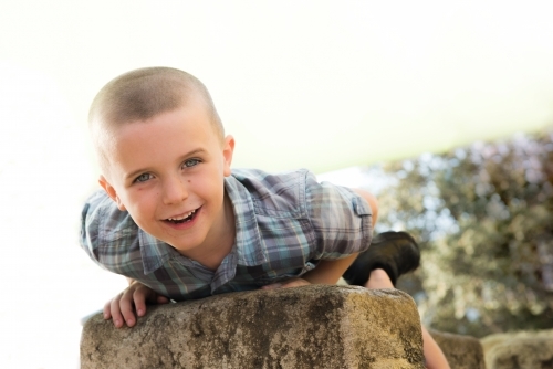 Child smiling at camera while laying on rock at park. - Australian Stock Image