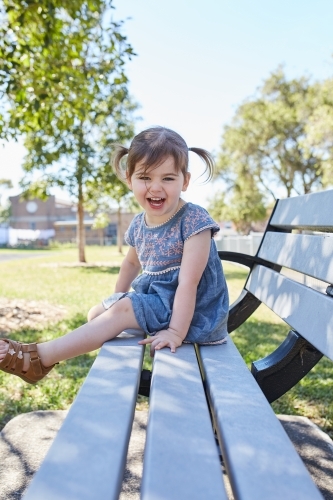 Child smiling on park bench wearing a blue dress - Australian Stock Image