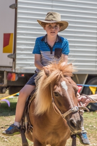 Child wearing akubra hat riding on horse - Australian Stock Image