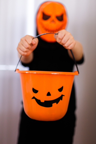 child wearing an orange mask holding out a halloween bucket - Australian Stock Image