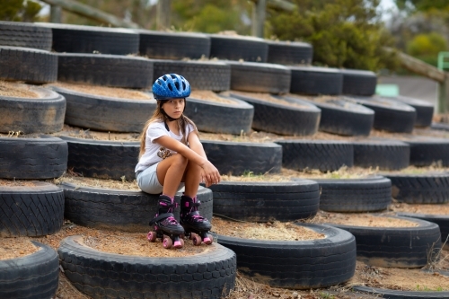 Child wearing blue helmet and roller skates sitting resting - Australian Stock Image