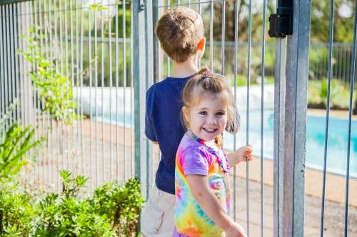 Children holding fence bars looking into pool yard - Australian Stock Image