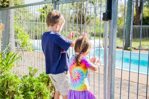 Children holding fence bars looking into pool yard - Australian Stock Image