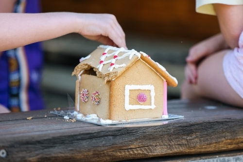 Children's hands pulling apart gingerbread house at Christmas time - Australian Stock Image