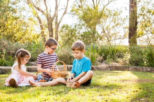 Children sitting on grass sorting out baskets of Easter eggs - Australian Stock Image