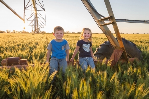 Children sitting on pivot irrigation system in wheat field paddock - Australian Stock Image