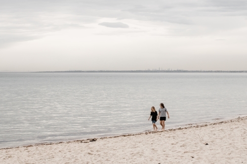 children walking along the beach with Melbourne City in the background - Australian Stock Image