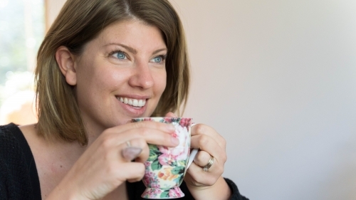 Close of young woman holding teacup looking away - Australian Stock Image