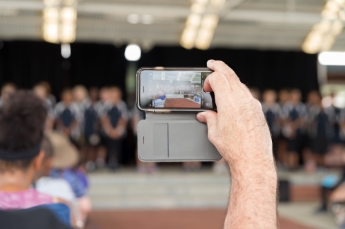 Close up Hand Holding Mobile Recording School Performance, Blurred - Australian Stock Image