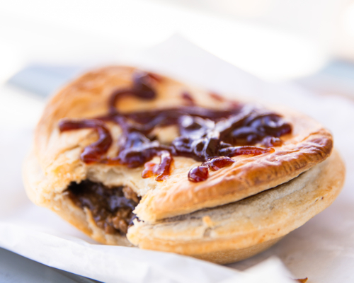 close up of a golden brown meat pie with sauce on top - Australian Stock Image