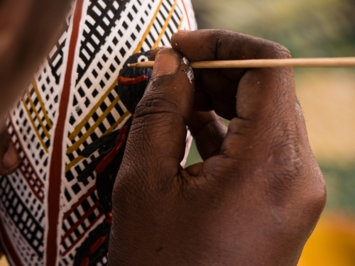 Close-up of a person’s hand holding a stick to apply colour on his craftwork. - Australian Stock Image