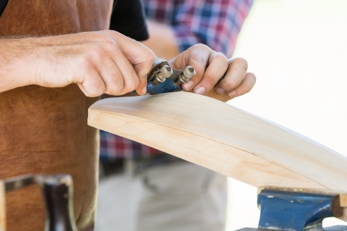 Close up of a tradesman's hands using a shaving tool over the back of cricket bat - Australian Stock Image