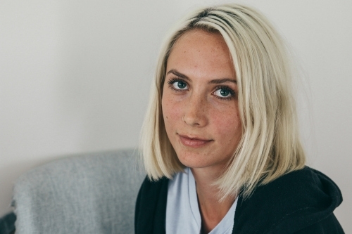 Close up of a young blonde woman looking up towards camera from a chair - Australian Stock Image