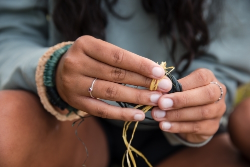 Close-up of an Aboriginal girl's hands as she is preparing threads for weaving baskets and bracelets - Australian Stock Image