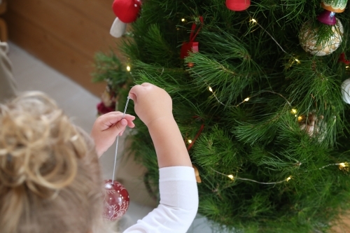 Close up of child's hands decorating Christmas tree - Australian Stock Image