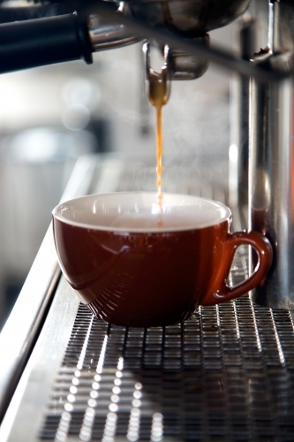 Close up of espresso coffee pouring into cup from coffee machine - Australian Stock Image