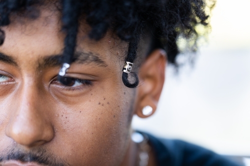 Close up of face of teenage boy with dark skin and beads in curly hair - Australian Stock Image