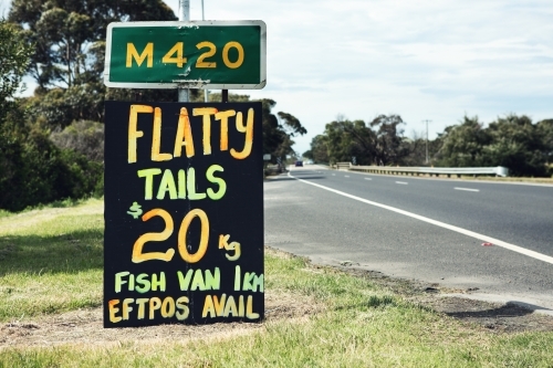 Close up of orange and yellow roadside sign advertising flathead tails - Australian Stock Image