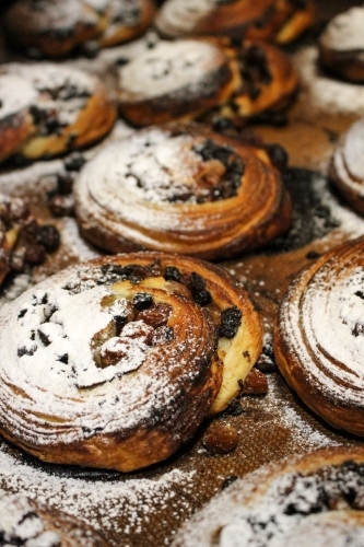 Close up of pain aux raisin pastries on baking tray dusted with icing sugar - Australian Stock Image