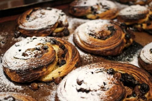 Close up of pain aux raisin pastries on baking tray dusted with icing sugar - Australian Stock Image