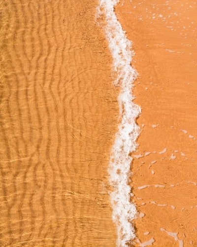 Close up of small wave over rippled sand - Australian Stock Image