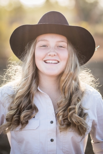 Close up of teenage girl wearing akubra hat smiling on farm in drought - Australian Stock Image