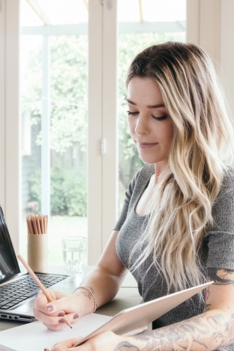 Close up of young blonde girl writing in a notebook at home - Australian Stock Image