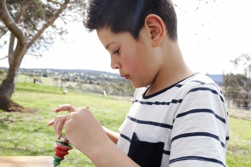 Close up of young boy doing Christmas craft outdoors - Australian Stock Image