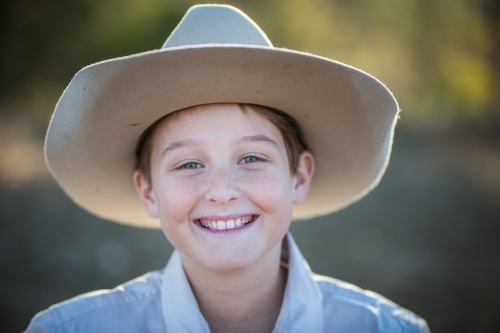 Close up of young boy smiling wearing akubra hat on farm in drought - Australian Stock Image