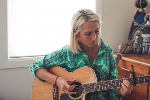 Close up of young woman looking down as she plays the guitar - Australian Stock Image