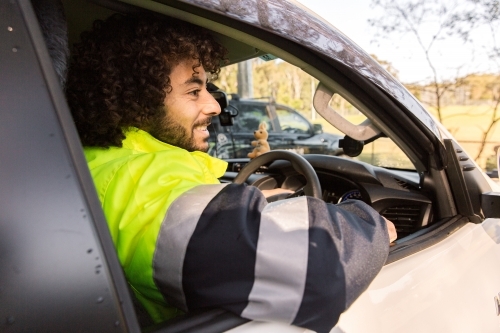 Close up photo of a man with curly hair wearing light green and grey jacket inside a black car