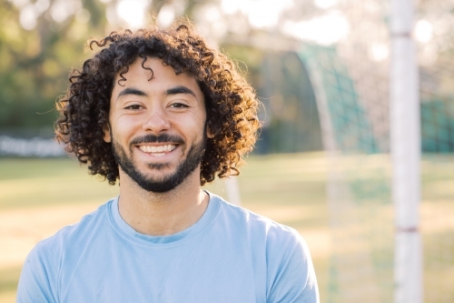 Close up photo of a smiling man with curly hair with beard wearing blue shirt on a sunny day - Australian Stock Image