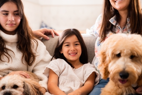 Close-up photo of a young girl smiling sitting next to her mum, sister and pet dogs at home