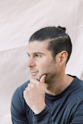 Close up photo of a young man with stylish hair looking on his left side with one hand on his face - Australian Stock Image