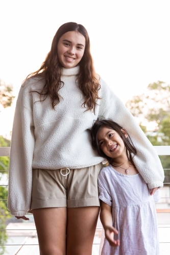 Close-up photo of little girl leaning on her teenage sister smiling - Australian Stock Image
