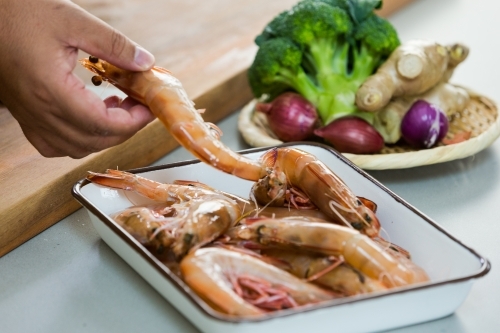 Close up photo of raw shrimp in a square shaped platter with broccoli, ginger and onions behind it - Australian Stock Image