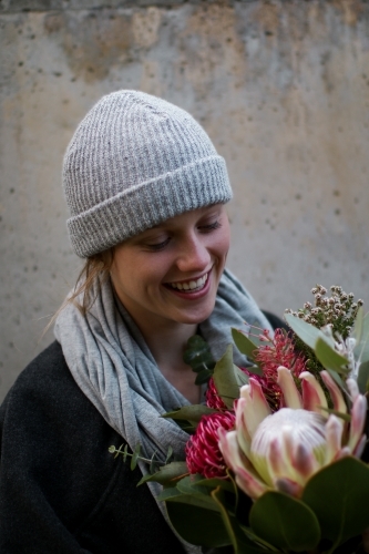 Close up portrait of young girl wearing a beanie and scarf smiling whilst holding a floral bouquet - Australian Stock Image