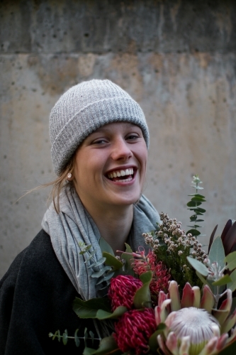 Close up portrait of young girl wearing a beanie and scarf smiling whilst holding a floral bouquet