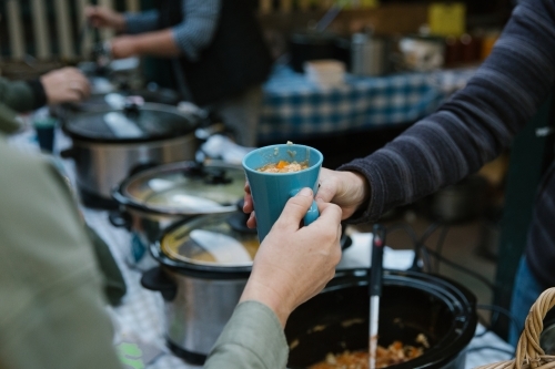 Close up shot of blue green cup with food inside being passed to another person - Australian Stock Image