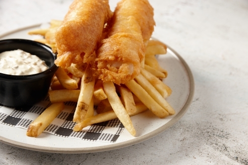 close up shot of fish and chips with buttermilk ranch dipping sauce all placed in  a white plate - Australian Stock Image