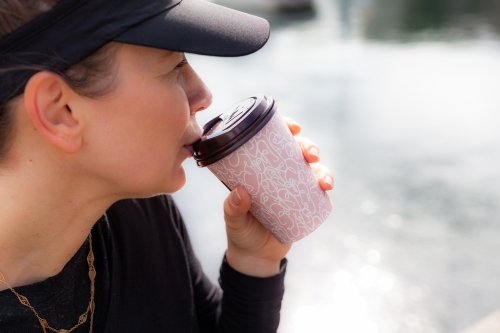 close up shot of woman wearing black shirt and black cap drinking coffee - Australian Stock Image