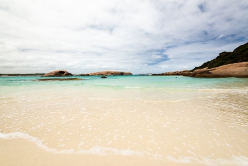 Close up view of water's edge at a pretty cove with swimmer in the distance and islands - Australian Stock Image